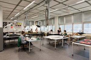 Ansicht eines Atelieraumes mit Personen die an ihren Tischen sitzen und mit technischen Geräten an Werken arbeiten
