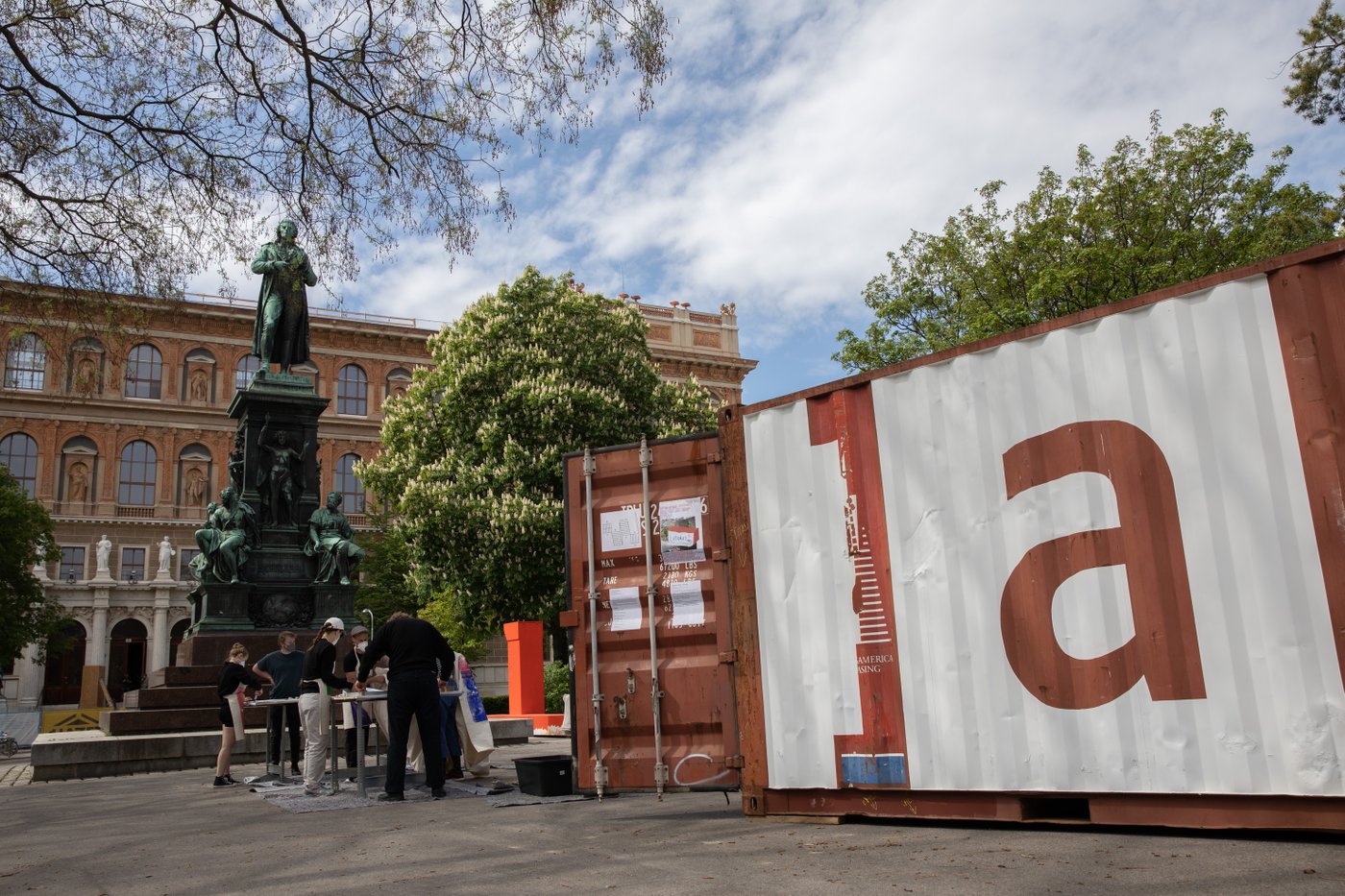 ESEL9659.jpg Baucontainer mit einem a und Studierende vor dem Schillerdenkmal