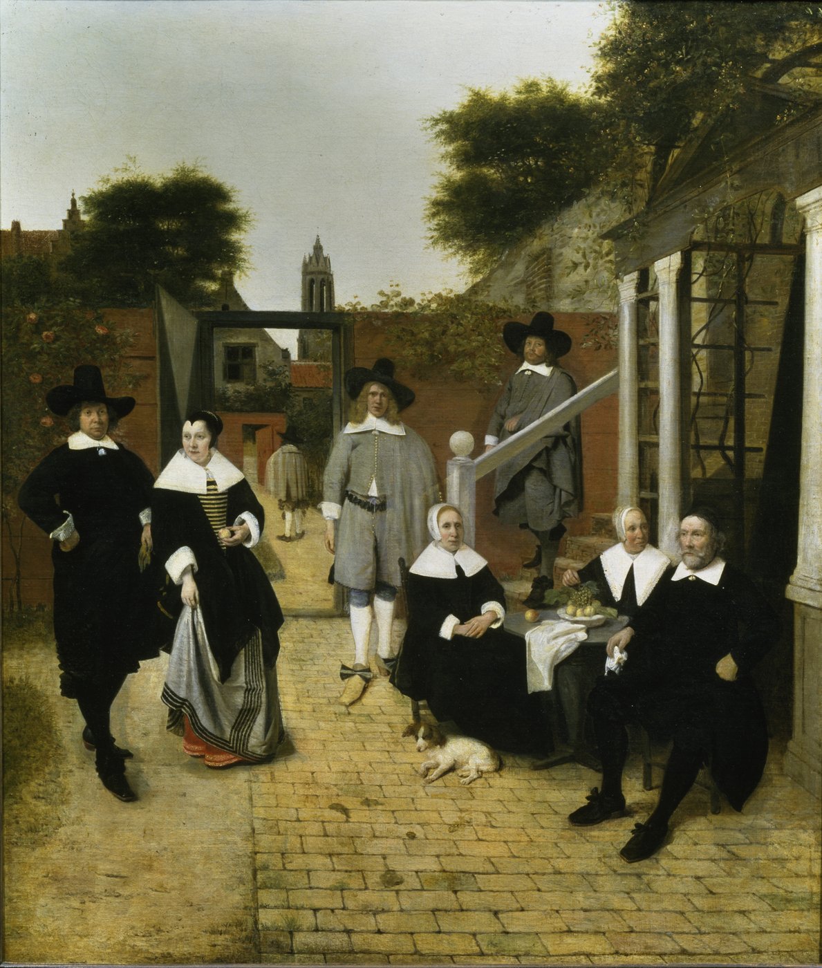 5a The painting is a depiction of a family grouped in a courtyard. The family members take different positions and postures. The younger ones are spread out in the courtyard, while the older ones are sitting together at a table. The portrayed people appear rigid and staged. Their stern postures reflect the straight lines of the courtyard walls and the architecture in the middle and background. All wear black or grey robes with large white collars and headdresses. Through the courtyard door, the view can glide backwards to a church tower. Every brushstroke seems to be thought out and controlled in order to reproduce the perspective, the architecture as well as the figures as realistic as possible.