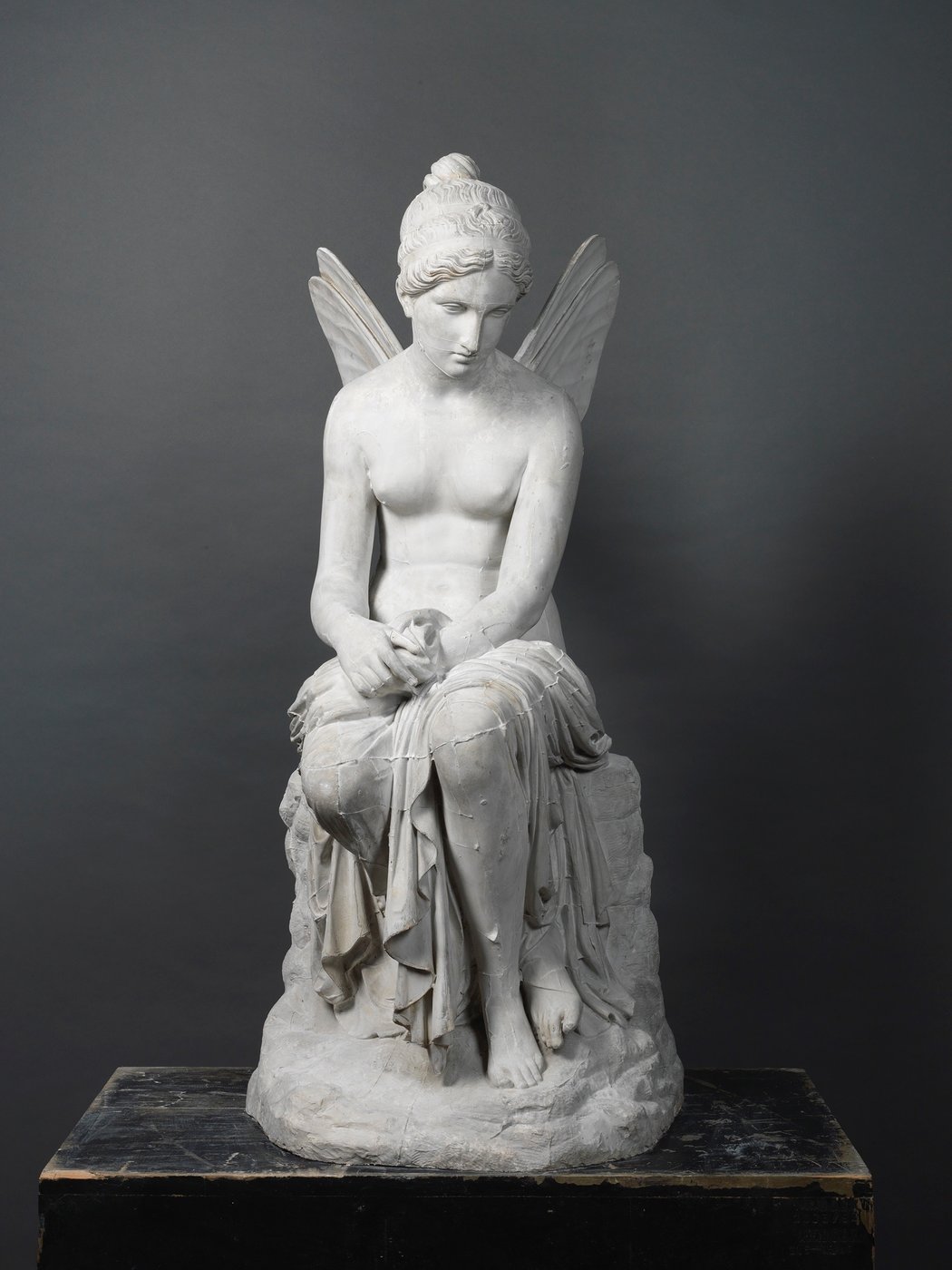 5 This black-and-white photograph presents a frontal view of the cast of a sculpture entitled Psyche Abandoned. The sculpture consists of a nude seated young woman with delicate wings on her back.