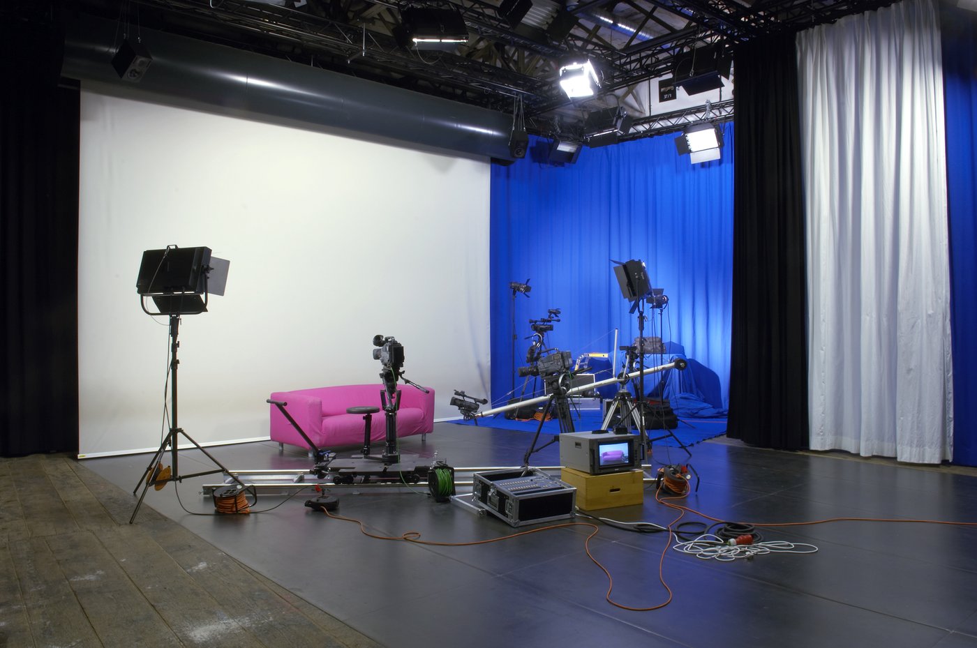 Blick in das Videostudio der Akademie, Foto © Lisa Rastl Ein typisches Videostudio mit einer Vielzahl von Kameras, Monitoren und anderen Gerätschaften. Ein rosa Sofa, an der Rückwand ein blauer Vorhang.