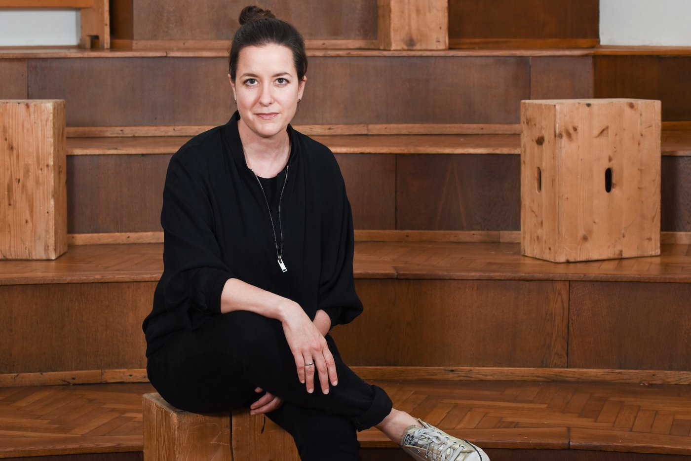 Picture of a woman in dark clothes with dark brown hair sitting on a wooden staircase