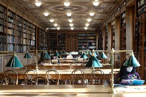 Historic reading room of the Academy of Fine Arts Vienna, designed by Theophil Hansen. Readers with laptops and FFP2 masks sit at sunlit tables.